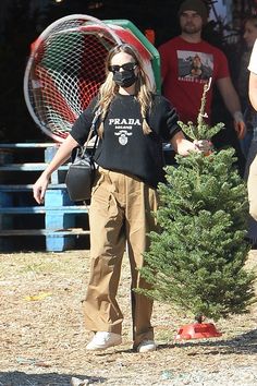 a woman wearing a face mask standing next to a small tree