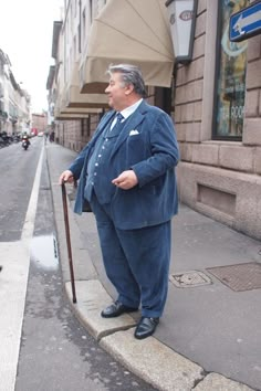 a man in a suit and tie standing on the side of a street with a cane