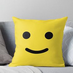 a yellow pillow with black eyes and a smiley face on the front, sitting on a couch