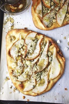 two pizzas with toppings sitting on top of a baking sheet next to a bowl