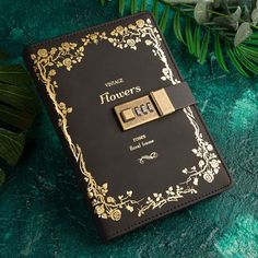 a black and gold binder with flowers on it next to some green leaves in the background