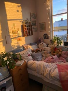 there are many stuffed animals laying on the bed in this room with sunlight coming through the windows