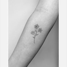 a black and white photo of a flower tattoo on the left inner arm, which has three small flowers growing out of it