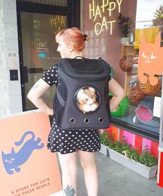 a woman is standing outside with her back to the camera and carrying a cat backpack