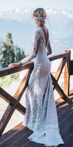 a woman in a white dress is standing on a wooden deck looking at the mountains