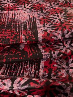 a red and black floral print fabric on a bed sheet with two matching pillows in the background