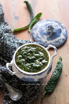 a bowl of pesto on a wooden table next to two spoons and a cloth