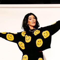 a woman in a black and yellow sweater with smiley faces on her shirt is posing for the camera