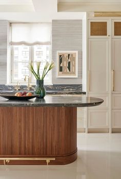 an elegant kitchen with marble counter tops and wooden cabinetry, along with two vases filled with flowers