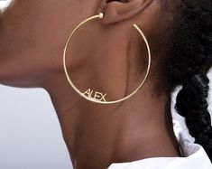 a woman wearing large gold hoop earrings with the word alex on it