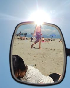 a woman is walking on the beach in front of a rear view mirror with her reflection