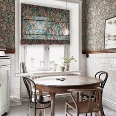 a dining room table and chairs in front of a window with roman shades on the windowsill