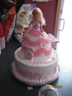 a barbie doll sitting on top of a pink and white birthday cake with the number six on it