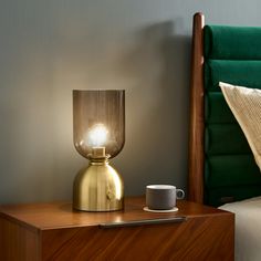 a nightstand with a lamp on it next to a green headboard and a bed