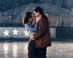 a man and woman embracing each other in the rain with stars on the ground behind them