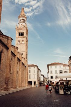 two people walking down the street in front of an old building with a clock tower