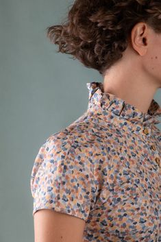 a woman with curly hair is wearing a floral shirt and has her back turned to the camera