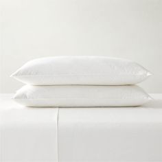 two pillows sitting on top of a bed with white sheets and pillow cases in front of them