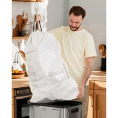 a man holding a large bag over a trash can in the middle of a kitchen