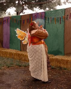 a woman dressed in an old fashioned dress and holding a butterfly on her shoulder while standing next to hay bales