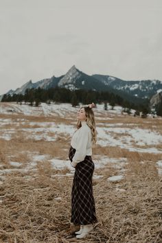 a woman standing in a field with mountains in the background