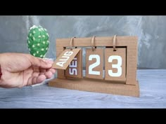 a hand holding a small wooden calendar with the date 23 on it and a cactus in the background