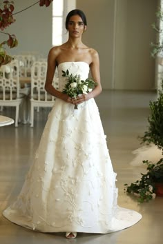 a woman in a white wedding dress holding a bouquet and standing on the floor with chairs behind her