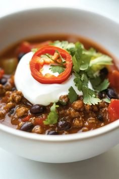 a white bowl filled with chili, beans and sour cream topped with cilantro