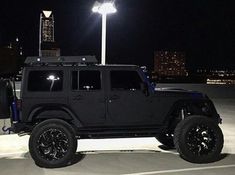 a black jeep parked in a parking lot at night with its lights on and the roof down