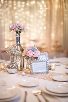 the table is set with silverware and pink flowers in vases on top of it