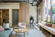 a living room filled with lots of furniture next to tall windows and potted plants