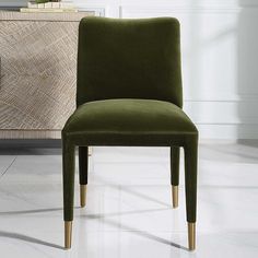 a green chair sitting on top of a white floor next to a wooden cabinet and lamp