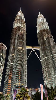 two very tall buildings in the middle of a city at night with lights on them