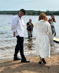 a man and woman standing on top of a beach next to the ocean with people taking pictures