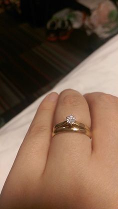 a woman's hand with a diamond ring on top of her finger in front of a bed