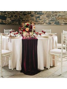 the table is set with white linens and red flowers on it, along with candles