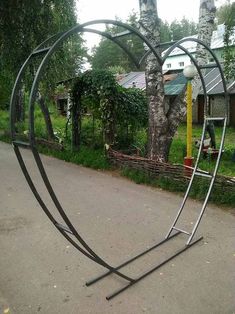 a heart shaped metal sculpture sitting on the side of a road next to a tree