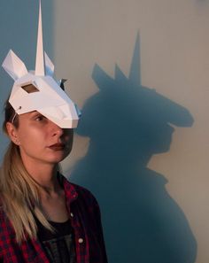 a woman standing in front of a wall with a paper mask on it's head