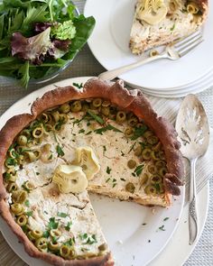 there is a pie on the plate with a slice taken out of it and salad in the background