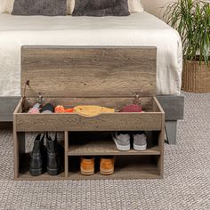 an open shoe box on the floor in front of a bed with two pairs of shoes