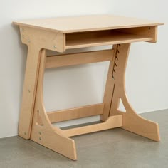 a small wooden desk sitting on top of a cement floor next to a white wall