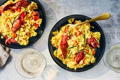 two black plates filled with pasta and lobster on top of a table next to a glass of wine