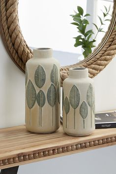 two vases sitting on top of a wooden shelf next to a roped mirror