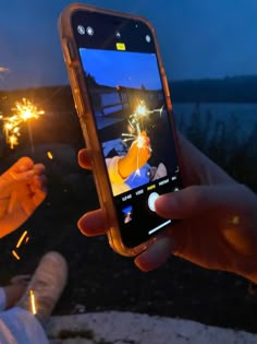 someone holding up their cell phone to take a photo with sparklers in the background