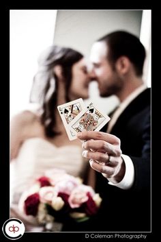 a bride and groom holding playing cards in their hands while the bride is kissing her