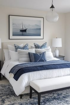 a bed with blue and white pillows in a bedroom next to a painting on the wall