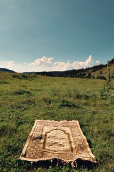 an old rug laying in the middle of a grassy field on a sunny day with blue sky and clouds