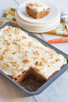 carrot cake with white frosting in a pan on a table next to plates and utensils