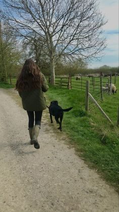 a woman walking down a dirt road with a dog