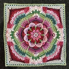 a crocheted square with a flower in the center on a black table top